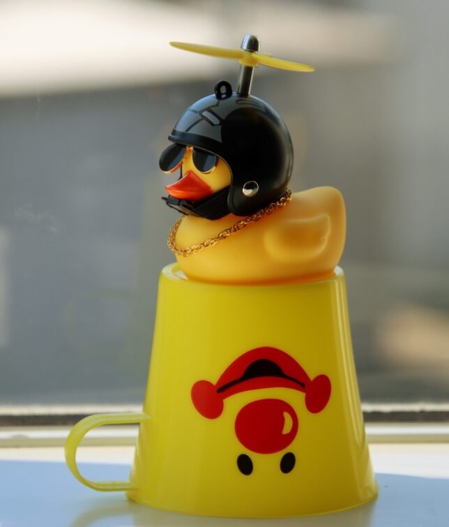 Yellow rubber duck in the helmet sitting on the clown cup